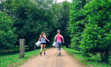 Two girls on back with garbage bags doing plogging