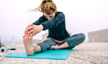 Young woman stretching legs on mat by sea pier
