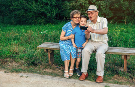 Grandfather taking selfie with grandmother and grandson sitting on a bench