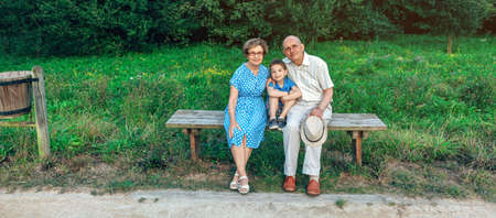 Grandparents and grandson posing for a photo sitting on a bench outdoors