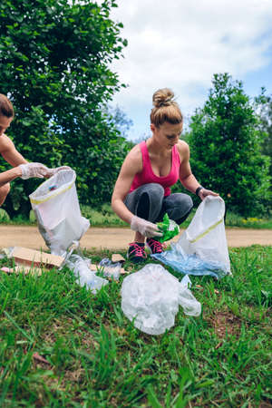 Girls crouching with garbage bag picking up trash doing plogging
