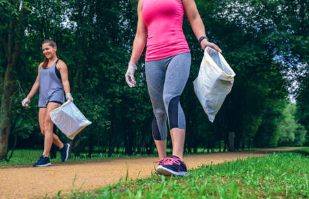 Happy girls with garbage bag picking up trash doing ploggingの写真素材