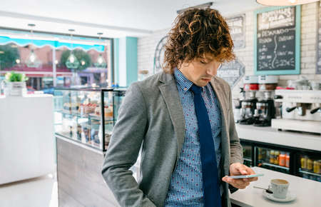 Businessman looking at mobile standing in a cafeの写真素材