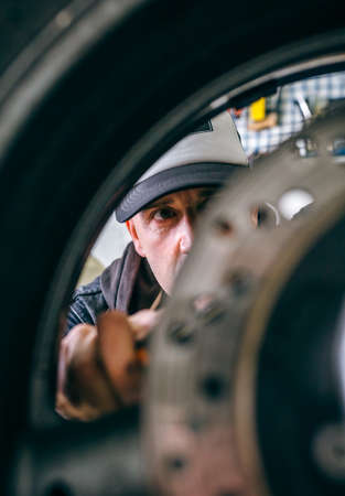 Mechanic fixing custom motorcycle wheel in his workshop. Selective focus on mechanic in backgroundの写真素材