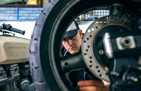 Mechanic fixing custom motorcycle wheel in his workshop. Selective focus on mechanic in backgroundの写真素材