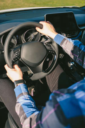 Detail of arms of young man holding the steering wheel while driving the car