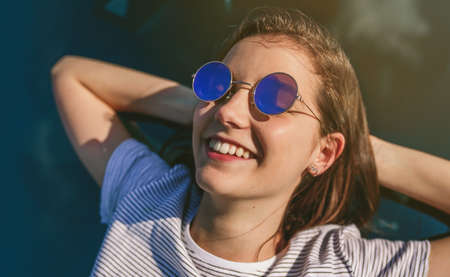 Happy young girl resting lying on the windshield of the car