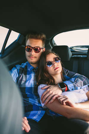 Young couple with sunglasses resting in the backseat of the carの写真素材