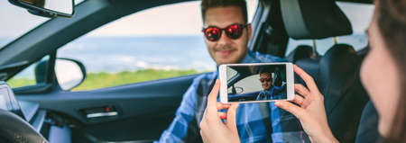 Girl taking a picture with the cell phone to her boyfriend in the car. Selective focus on mobile in foregroundの写真素材