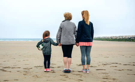 Back view of three generations female watching the sea in autumnの写真素材