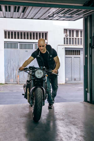 Front view of biker taking custom motorbike to the garage