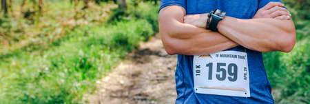 Young male trail athlete posing with race number placed outdoors