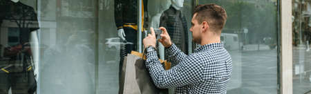 Young man taking a photo of a mannequin from a shop window of a fashion storeの写真素材