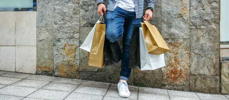 Unrecognizable young man with shopping bags leaning on a stone wallの写真素材
