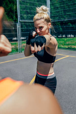 Young sportswoman training boxing with her trainer outside