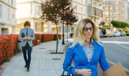 Serious businesswoman walking down the street towards her work while a businessman walks behind....