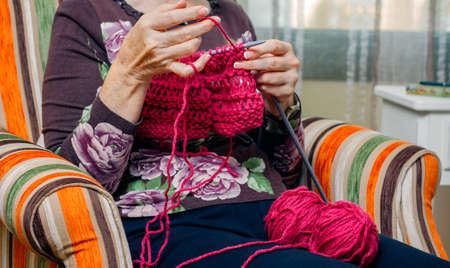 Hands of senior woman knitting a wool sweater at home