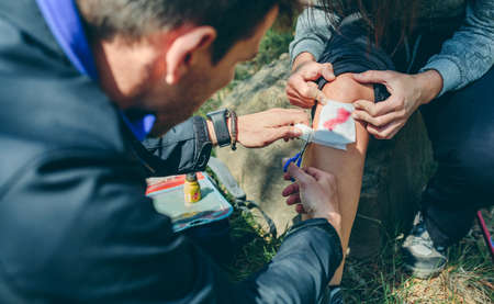 Young man healing knee to a young woman who has been injured doing trekkingの写真素材