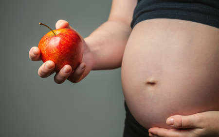 Belly of pregnant woman holding a red apple