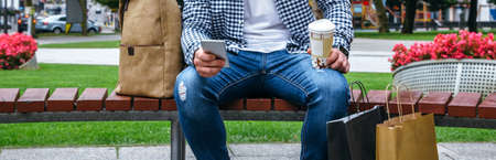 Young man with cell phone looking camera sitting on a park benchの写真素材