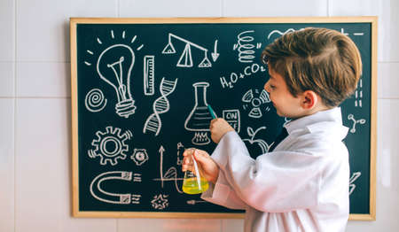 Smiling boy dressed as chemist with flask pointing at a blackboard with drawings