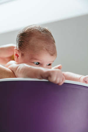 Newborn girl in the bathtub held by her mother upside downの写真素材