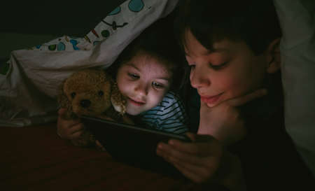 Brother and sister lying on the bed looking at the tablet in the darkの写真素材