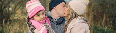 Closeup of happy couple with her little daughter kissing over a forest background. Focus on couple.の写真素材