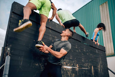 Group of participants in an obstacle course climbing a wallの写真素材