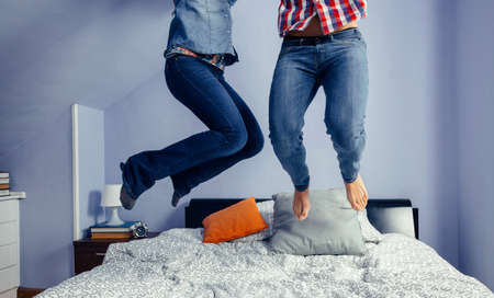 Legs of unrecognizable happy couple jumping on the bed indoors