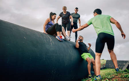 Group of participants in an obstacle course going down a drum helped by their teammatesの写真素材