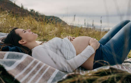 Pregnant woman caressing her naked tummy sleeping on the grassの写真素材
