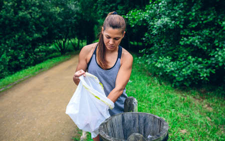 Young woman throwing garbage into a trash can after ploggingの写真素材