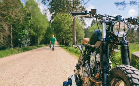 Custom vintage motorbike on the side of the road with guy in the background walking with gasoline...