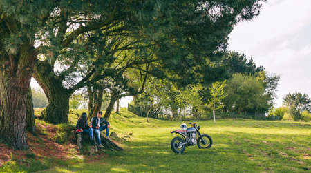 Young couple resting from a motorcycle trip having a beer outdoors