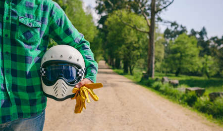 Unrecognizable young man posing with motorcycle helmet and gloves in the middle of the roadの写真素材