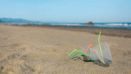 Beach landscape with plastic cups and straws after party
