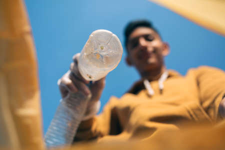 Young man throwing plastic bottles in the trash. Selective focus on bottle in the foregroundの写真素材