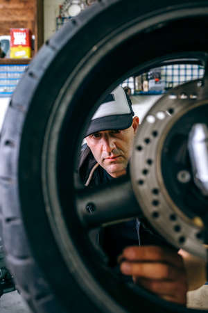 Mechanic fixing custom motorcycle wheel in his workshop. Selective focus on mechanic in backgroundの写真素材