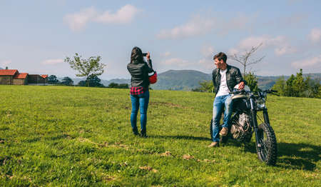 Young couple making a landscape photo during a stop of a motorcycle trip