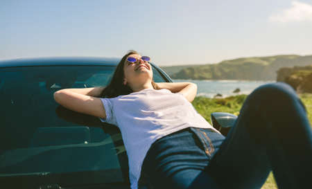 Happy young girl resting lying on the windshield of the car