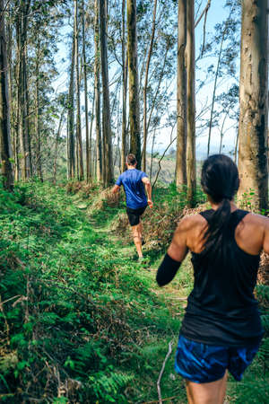Young woman and man participating in a trail race through the forestの写真素材