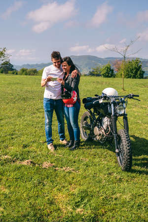 Young couple looking mobile with a motorcycle outdoors