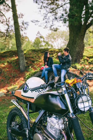 Custom motorbike with young couple resting from a motorcycle trip in background. Selective focus on motorbike in foregroundの写真素材