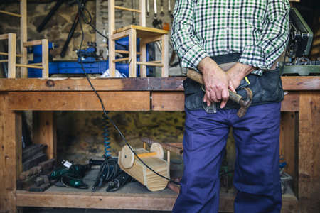 Unrecognizable senior carpenter posing with a hammer