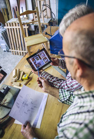 Senior couple working in a carpentry workshop looking tablet with chair design
