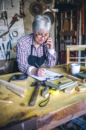 Senior female carpenter talking on the phone in his workshopの写真素材