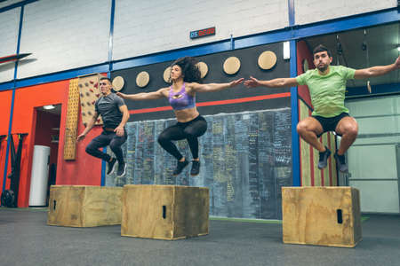 Group of athletes exercising jumping wooden box in the gymの写真素材