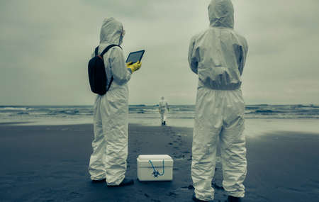 Unrecognizable people with bacteriological protection suits looking for evidence at seaの写真素材