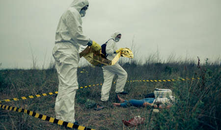 Man and woman in bacteriological protective suits covering a womans body with a thermal blanket